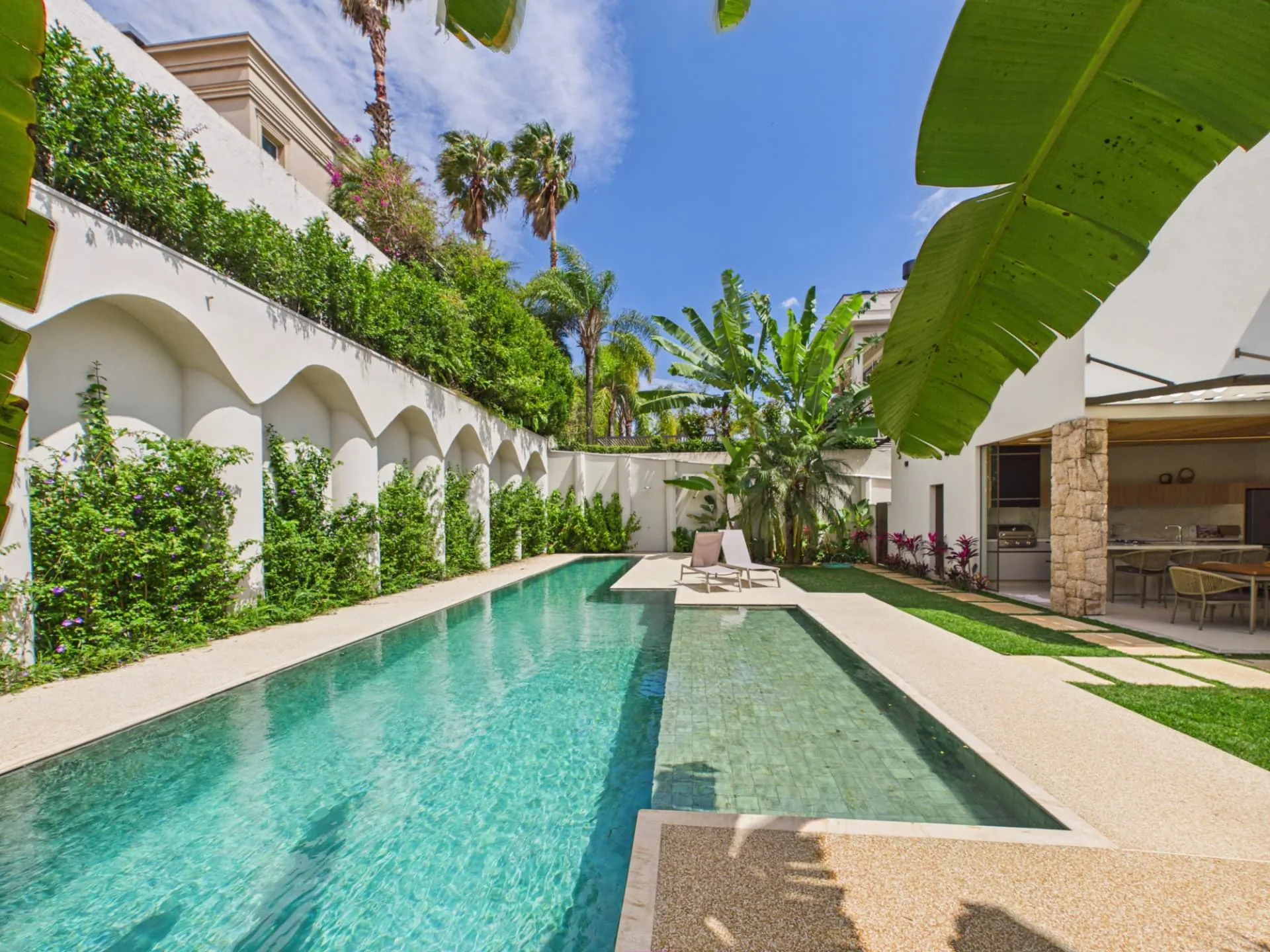Piscina com raia e paredes em arcos integradas ao jardim