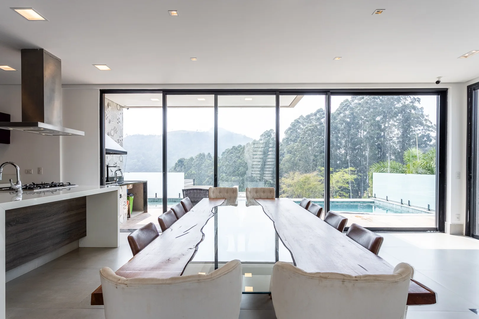 Cozinha integrada à sala de jantar com vista para a piscina e a mata